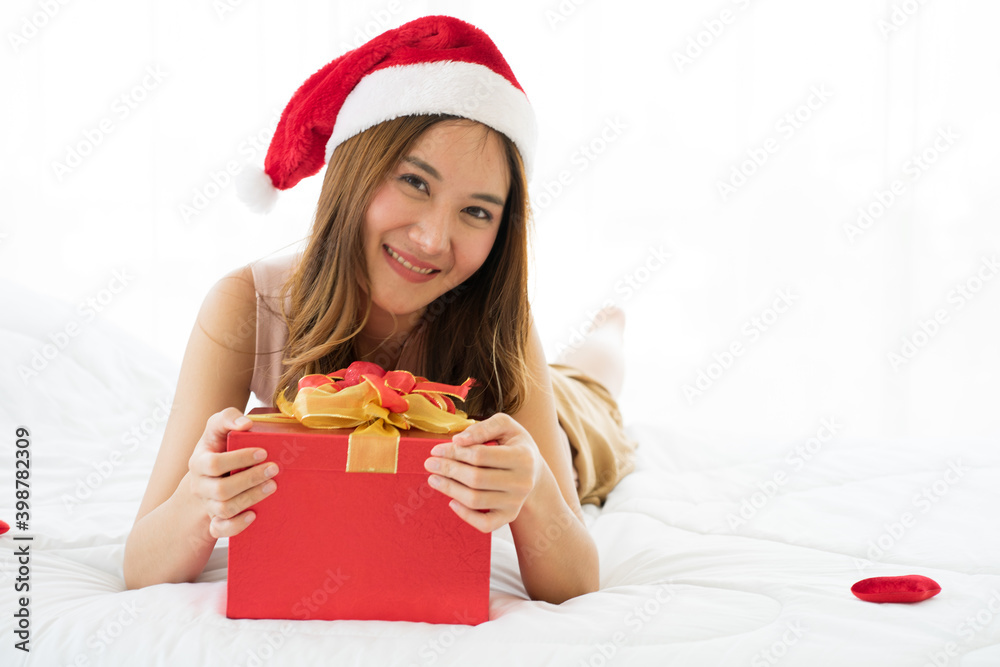 Asian Attractive young Wolman on bed wearing red Santa hat and red gift box during Christmas holiday. new normal concept. Asian Attractive young Wolman on bed wearing red Santa hat and red gift box during Christmas holiday. new normal concept.