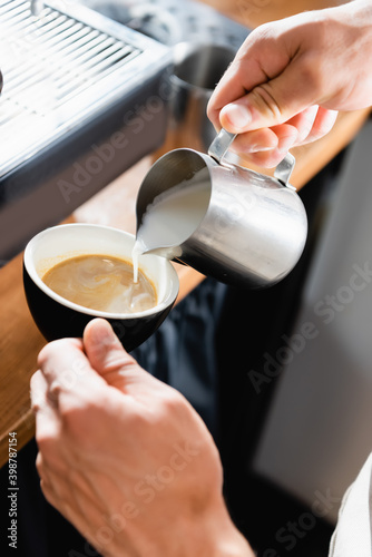 cropped of barista pouring milk from metallic mug into cup with coffee