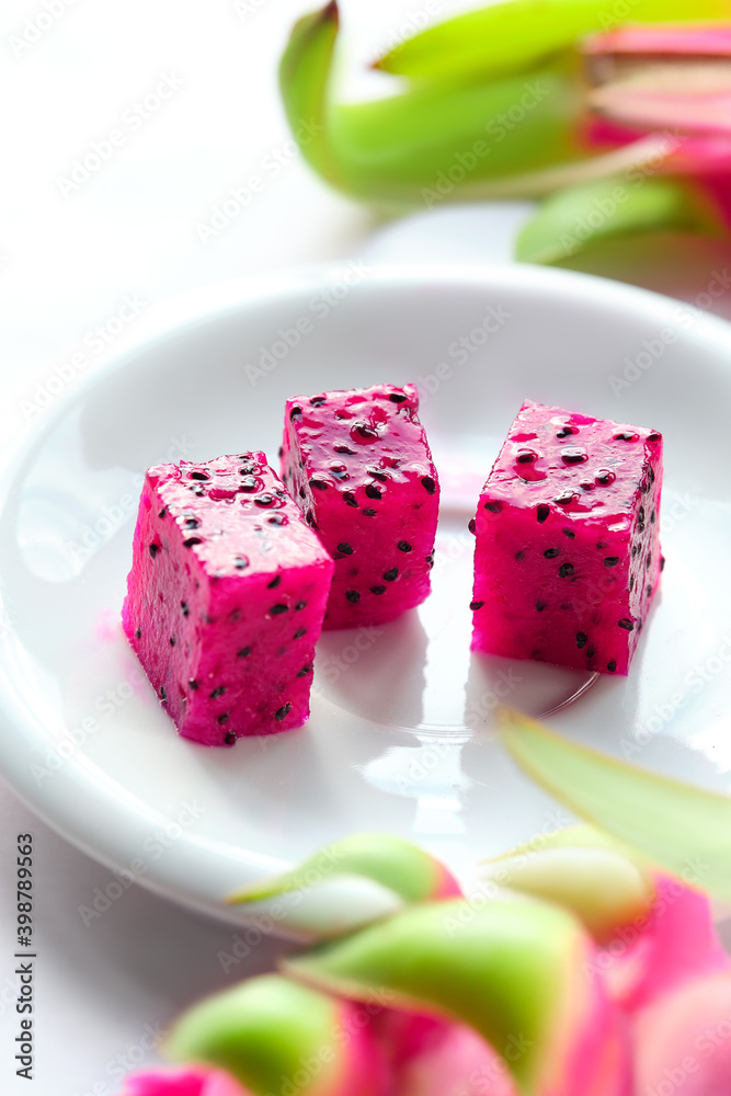 Pink dragon fruit, pitaya or pitahaya cut in cubes on white plate. Trendy superfood ingredient. Close-up image, shallow DOF, focus on the cubes.