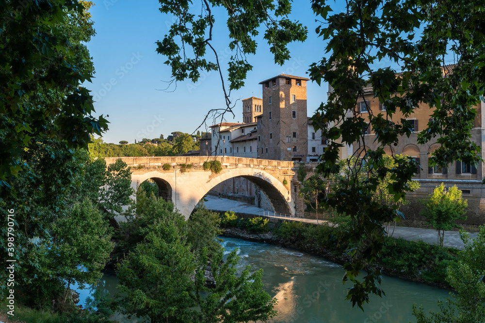 Rome Isola Tiberina, Ponte Fabricio from the Lungotevere dei Cenci, called the bridge of the 4 heads in travertine formed by large arches. Beautiful reflections of the luxuriant tiber vegetation.