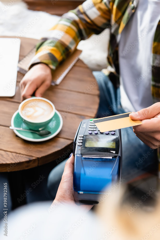 cropped of waiter holding payment terminal and man with credit card sitting at table with cup of coffee