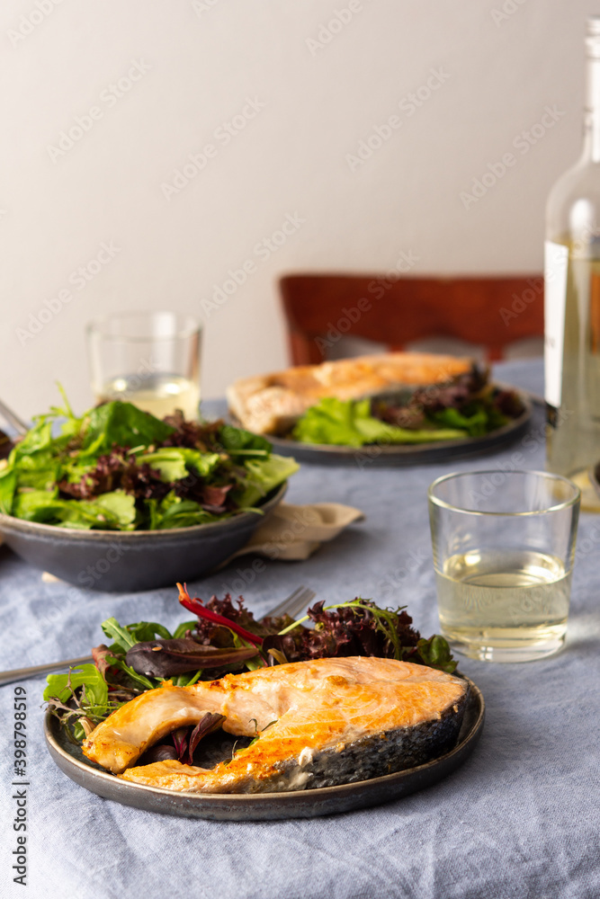 Fried salmon steak with salad in a plate , white wine in a glass, delicious hearty dinner or lunch