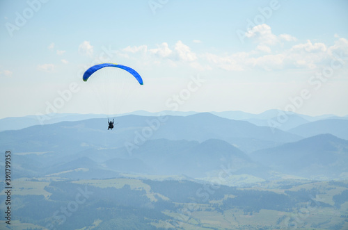 Paraglider flying over the mountains against the blue sky in clear weather. Extreme sport, lifestyle and freedom concept