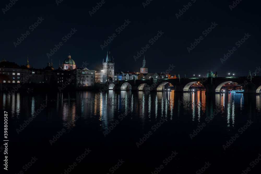 Charles Bridge from 14 centuries and light from street lighting and stone sculptures on the bridge and light reflections on the surface of the Vltava river at night in Prague