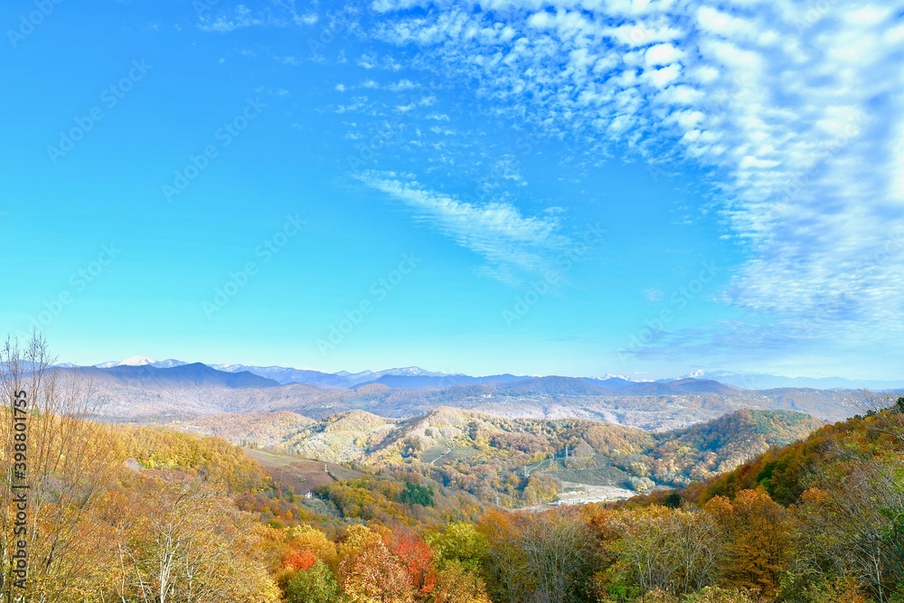 Panorama of mountain peaks to the horizon, covered with mixed forest, with a village on the slopes