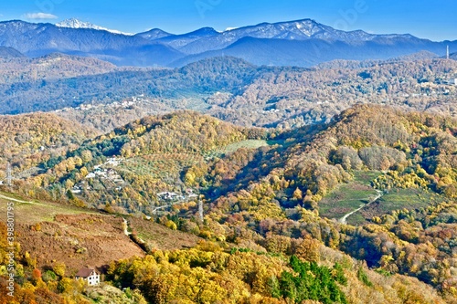 Panorama of mountain peaks to the horizon, covered with mixed forest, with a village on the slopes