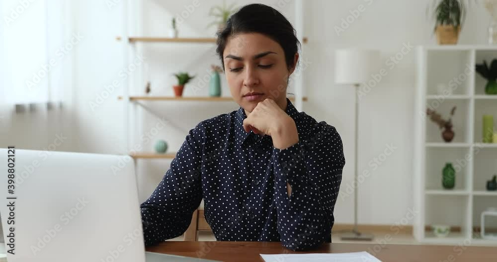 Attractive Indian businesswoman working on laptop sit at workplace at home or office room. Develop start up, search and create new fresh ideas, think over business plan texting on portable computer
