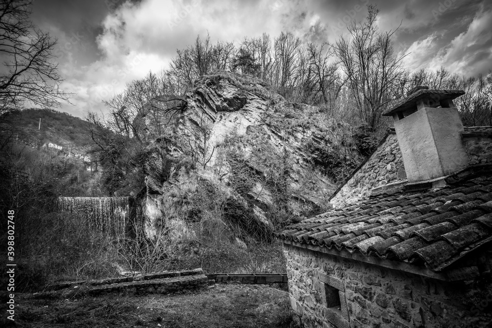 Black and white effect of waterfall in a valley with an ancient house, Caglieron caves, Veneto, Italy Black and white effect of waterfall in a valley with an ancient house, Caglieron caves, Veneto, Italy