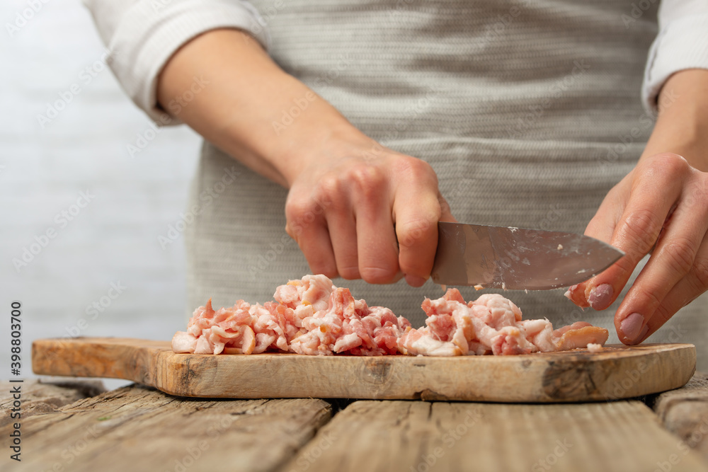 Close-up view of chef cuts with knife bacon on wooden board for cooking pasta alla carbonara. Backstage of preparing traditional italian dish on white background. Frozen motion. Cookbook illustration.