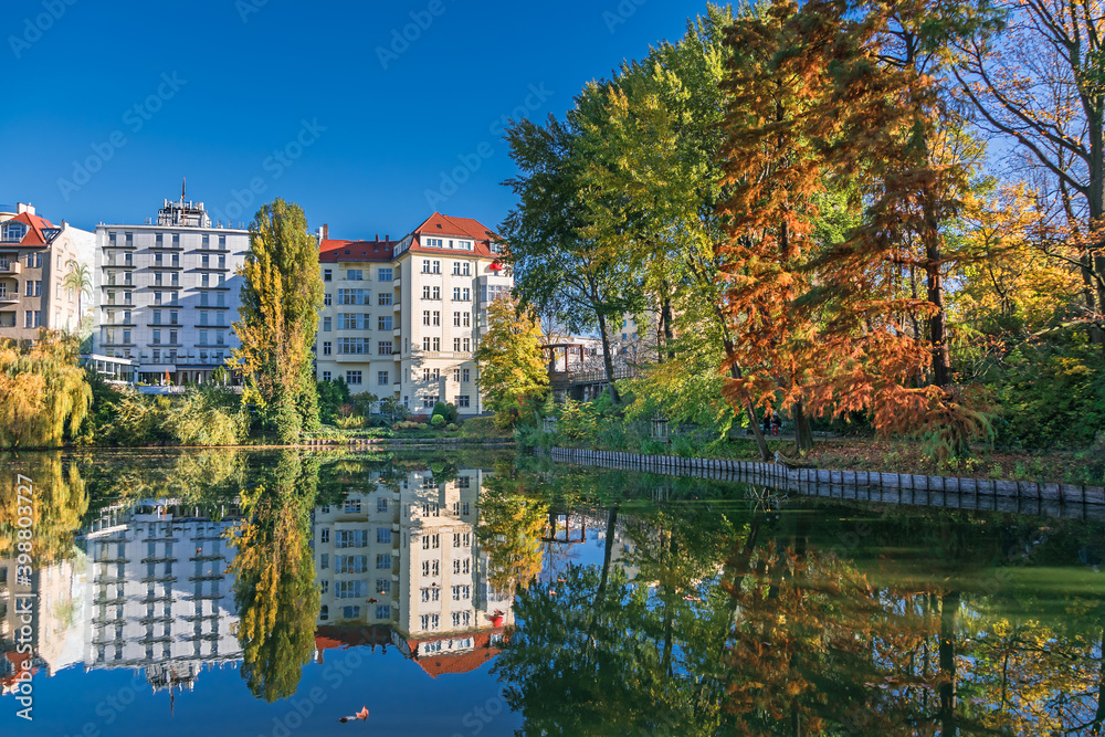 Park at the shore of Lake Lietzen with buildings reflecting in the water and the Lake Lietzen bridge in Berlin, Germany