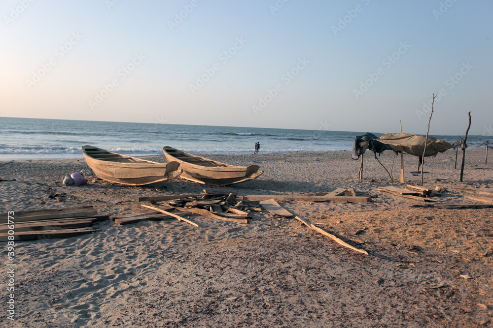 horizontal wide angle photography of a sea shore landscape, with wooden handmade boats and shade shelter made of palm trees, on an Atlantic beach, outdoors oj a sunny day in the Gambia, Africa horizontal wide angle photography of a sea shore landscape, with wooden handmade boats and shade shelter made of palm trees, on an Atlantic beach, outdoors oj a sunny day in the Gambia, Africa