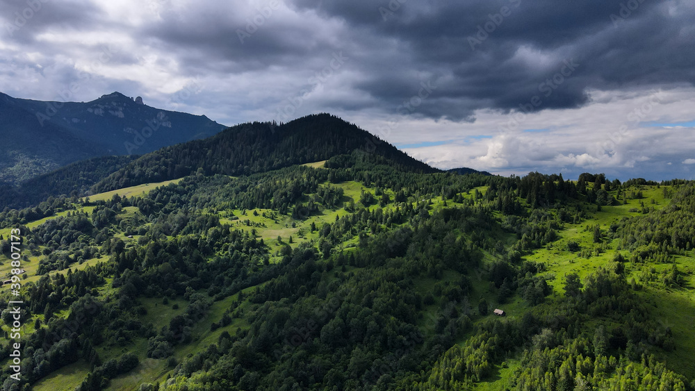 Green hills with scattered trees at the base of Mount Ceahlau - Romania with Toaca Peak in background Green hills with scattered trees at the base of Mount Ceahlau - Romania with Toaca Peak in background