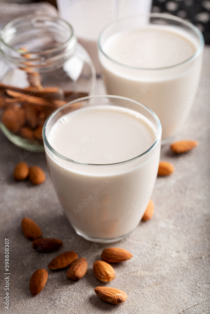 Homemade organic almond milk in a glass on stone background with cinnamon sticks.