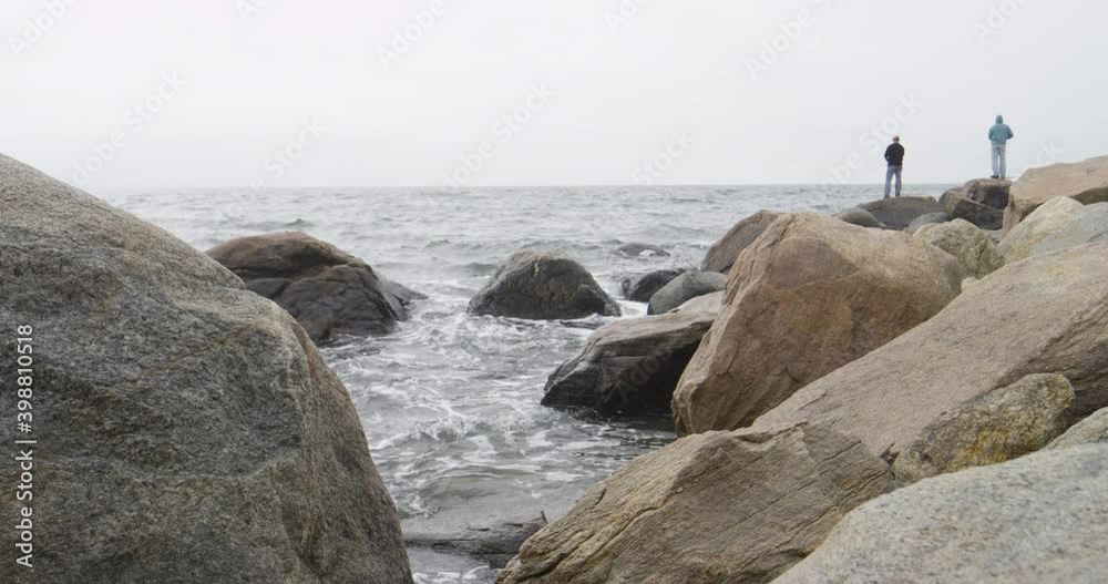 A rocky Atlantic ocean seashore with fishermen in the distance in a cloudy day A rocky Atlantic ocean seashore with fishermen in the distance in a cloudy day