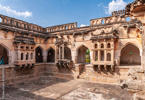 Hampi, Karnataka, India - November 4, 2013: Queens bath structure of Vijayanagara Empire. Wide view on 3 brown stone balconies, one damaged, over dry pool in corner of structure. Black mold and blue s photo