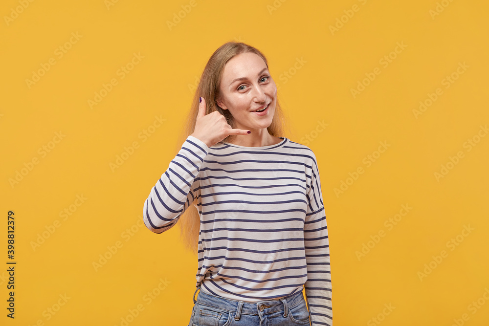 A portrait of a happy young beautiful woman shows a call me back gesture. Yellow background. A portrait of a happy young beautiful woman shows a call me back gesture. Yellow background.