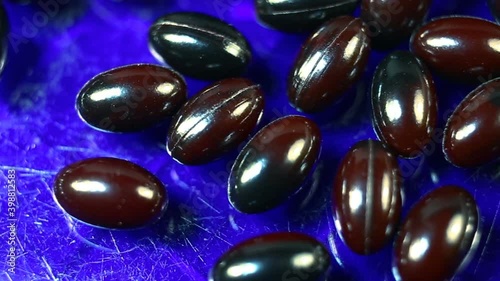 Maroon and black oval spindle-shaped capsules in a gel shiny shell extremely close-up moves from bottom to top and from top to bottom. Real time, natural light, on a blue background, carotenoids, caro photo