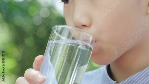 4k Selective focus, close up young Asian boy drink water from glass in the garden