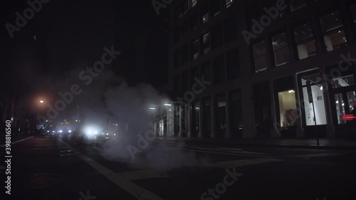 Silhouetted traffic in New York City at night driving through steam coming out of the ground. Classic ominous NYC traffic shot.