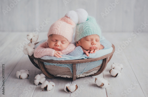 Twins are newborn brother and sister. Newborn girl and boy. Hats with white fur balls sleep sweetly in a basket.