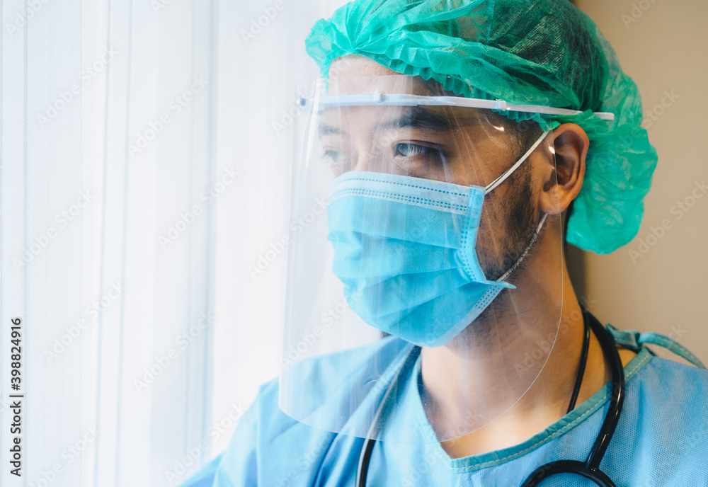 Asian male doctor wearing medical gown with face shield and mask before working in operating room in hospital.