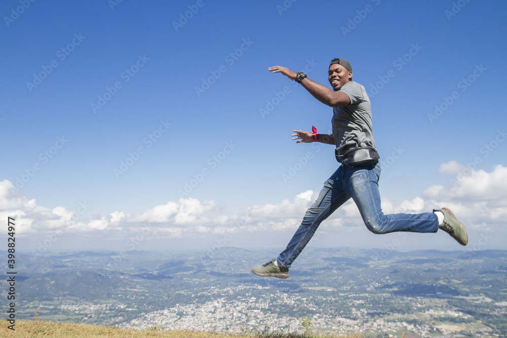 full body shot of one black skinned latin or african american young man outdoors jumping high looking to camera in a summer day vacation trip with nature blue sky in background full body shot of one black skinned latin or african american young man outdoors jumping high looking to camera in a summer day vacation trip with nature blue sky in background