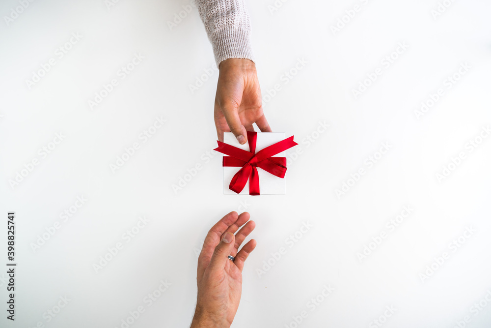 Beautiful holiday or Christmas background image of a mixed race African American woman handing a small red ribbon wrapped gift box to a Caucasian male's open hand on a white backdrop with copy space. Beautiful holiday or Christmas background image of a mixed race African American woman handing a small red ribbon wrapped gift box to a Caucasian male's open hand on a white backdrop with copy space.