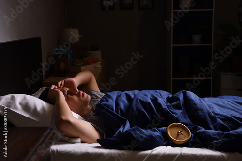 A depressed young man suffering from insomnia lying in bed..