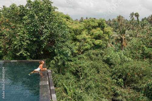 Young woman in swimsuit relaxing in the infinity pool with jungle view during vacation retreat in tropical country