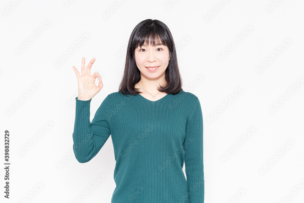 白背景の前に立ってOKのジェスチャーをする女性 白背景の前に立ってOKのジェスチャーをする女性