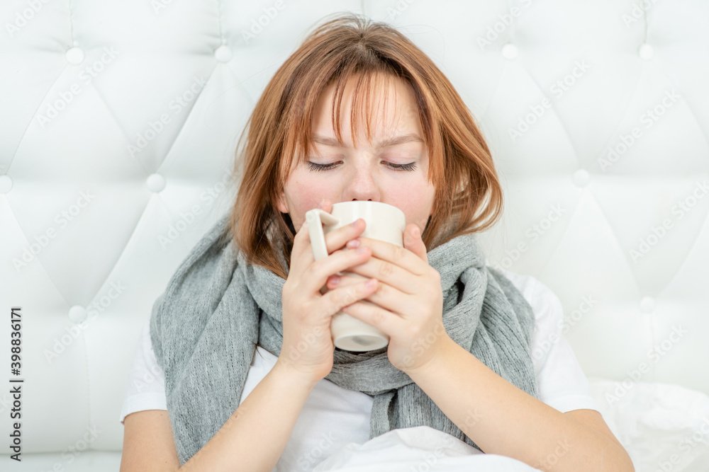Sick girl sits on a bed at home and drinks hot tea from a mug Sick girl sits on a bed at home and drinks hot tea from a mug