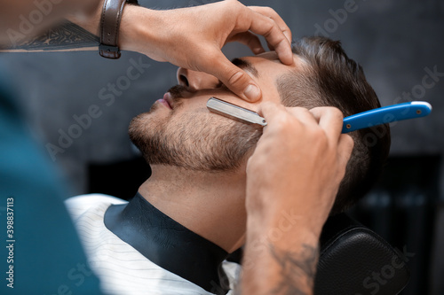 Hairdresser shaving client in barbershop