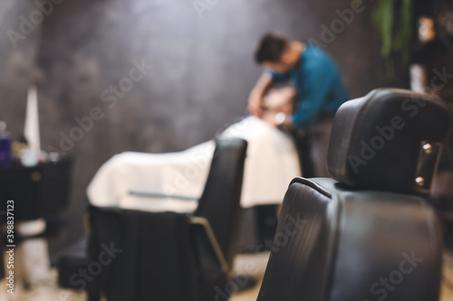 Hairdresser shaving client in barbershop, blurred view