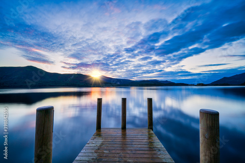 Vibrant sunset with dramatic clouds and wooden jetty at Derwentwater Lake in the Lake District  UK.