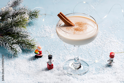 Christmas cocktail eggnog in a beautiful glass on a blue background covered with snow, horizontal orientation