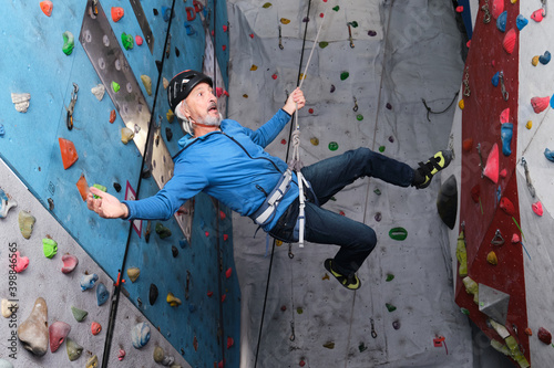 Professional senior man flying after jump while he is climbing on an artificial rock climbing wall. Extreme sports concept. photo