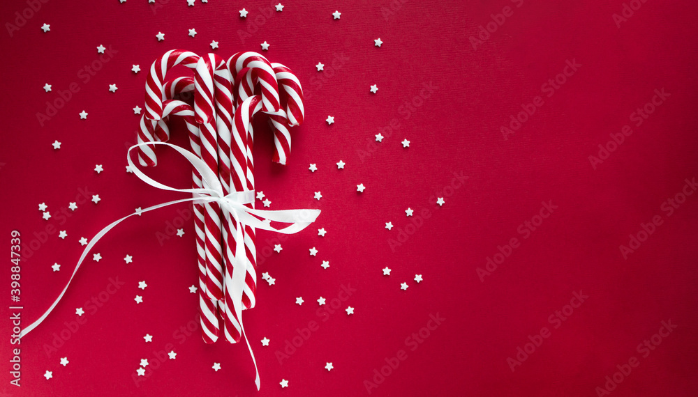 Christmas horizontal background with candy canes. Red sweet sticks with white ribbon. Flat lay, overhead view, copy space. Poster, banner, greeting card template. Festive backdrop. Holiday season Christmas horizontal background with candy canes. Red sweet sticks with white ribbon. Flat lay, overhead view, copy space. Poster, banner, greeting card template. Festive backdrop. Holiday season