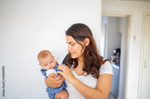 Woman holding her adorable baby inside a white bedroom
