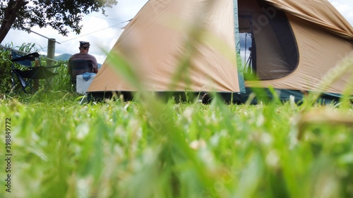 An Asian male tourist sits on a chair next to a tent, the green grass in the foreground, travel concept.