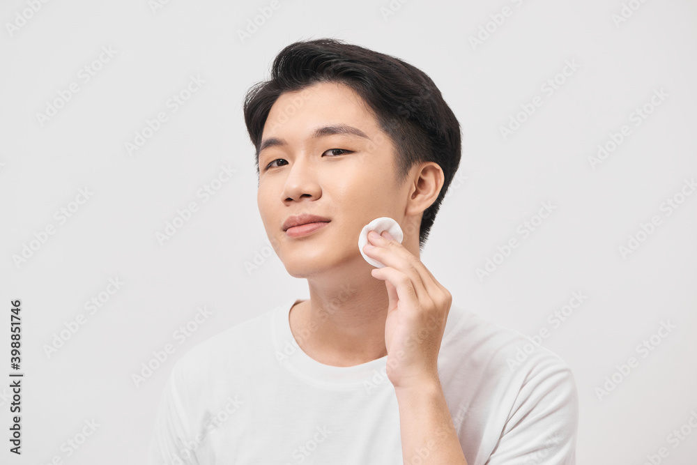 Beauty portrait of confident young man using cotton pad on his face isolated over white background Beauty portrait of confident young man using cotton pad on his face isolated over white background