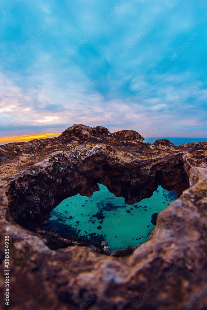 Sunset sky, a hole in the rock through which you can see the clear turquoise sea. Sea Wallpaper for the background. Winter at sea. Vertical photo