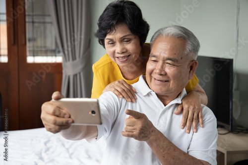 Happy old asian senior couple using smartphone for video call, selfie, taking photo