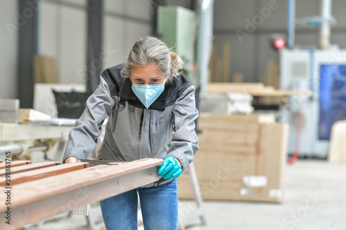 Woman worker operating in the carpentry workshop and wearing protections againt covid-19