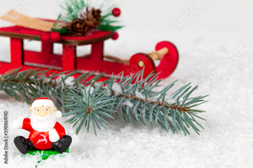 toy santa claus, sleigh and blue spruce branch with needles on a background of white snow