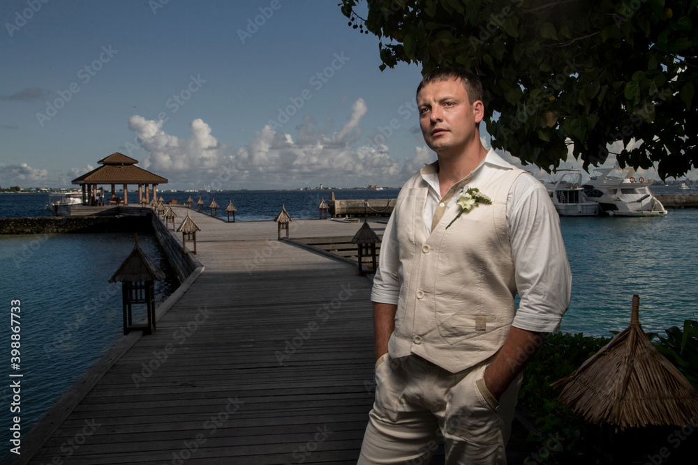 Young groom in white clothes at the sea in the Maldives