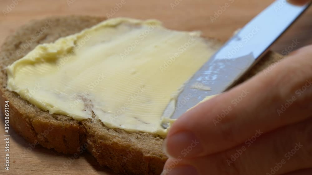 Close-up butter spreading on rustic rye bread with metal knife on wooden table Close-up butter spreading on rustic rye bread with metal knife on wooden table