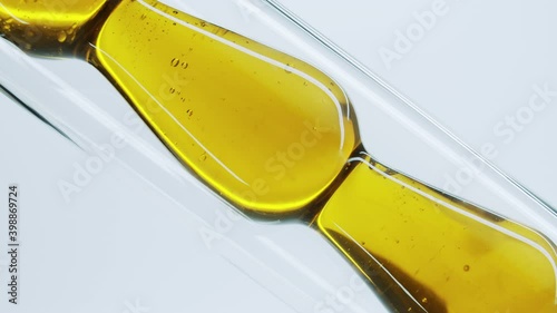 Yellow natural oil flows through a laboratory glass tube. Obtaining essential oils by filtration. Production of natural cosmetics. Сlose-up of glass test tube with oil.