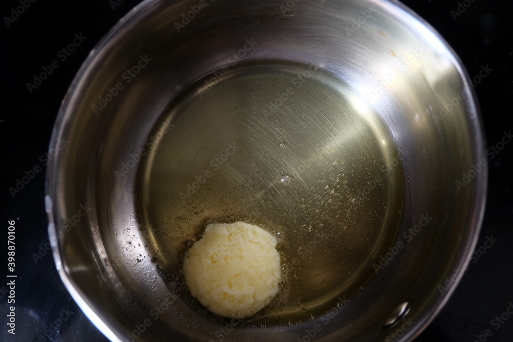 Butter in a pot. One spoon of butter pat melting on an iron frying pan. It is called Butter in a pot. One spoon of butter pat melting on an iron frying pan. It is called