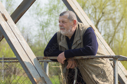 Portrait of Caucasian senior man with walking stick standing on an metal pedestrian bridge and looking at the distance