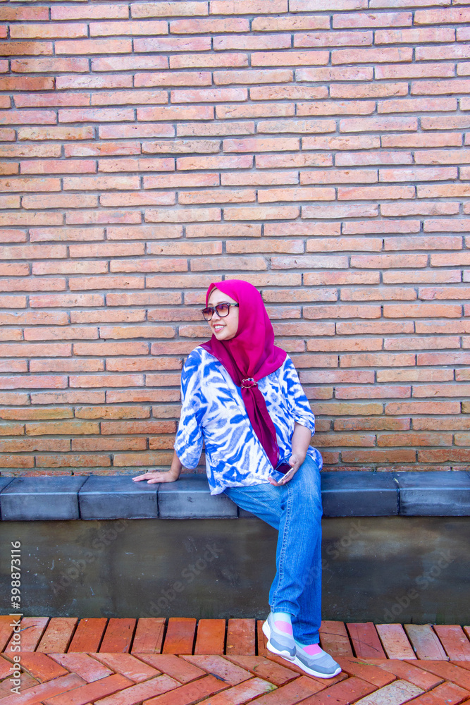 Asian muslim woman 50S with sun glasses sitting on brick wall Asian muslim woman 50S with sun glasses sitting on brick wall